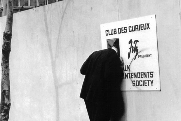 Un homme regarde dans une ouverture placée dans une affiche du Club des curieux.