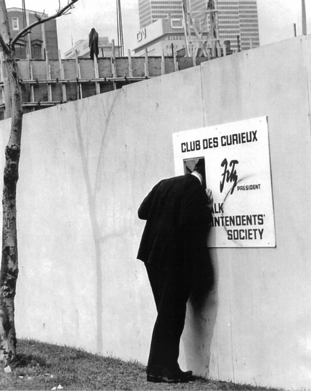 Un homme regarde dans une ouverture placée dans une affiche du Club des curieux.
